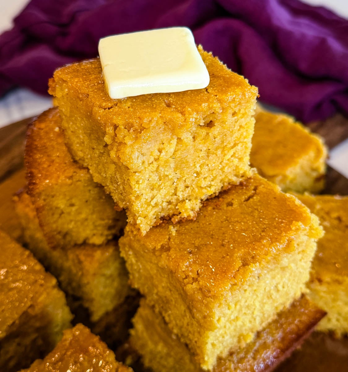 Close-up of moist honey butter cornbread stacked high with a pat of butter melting on the top piece.