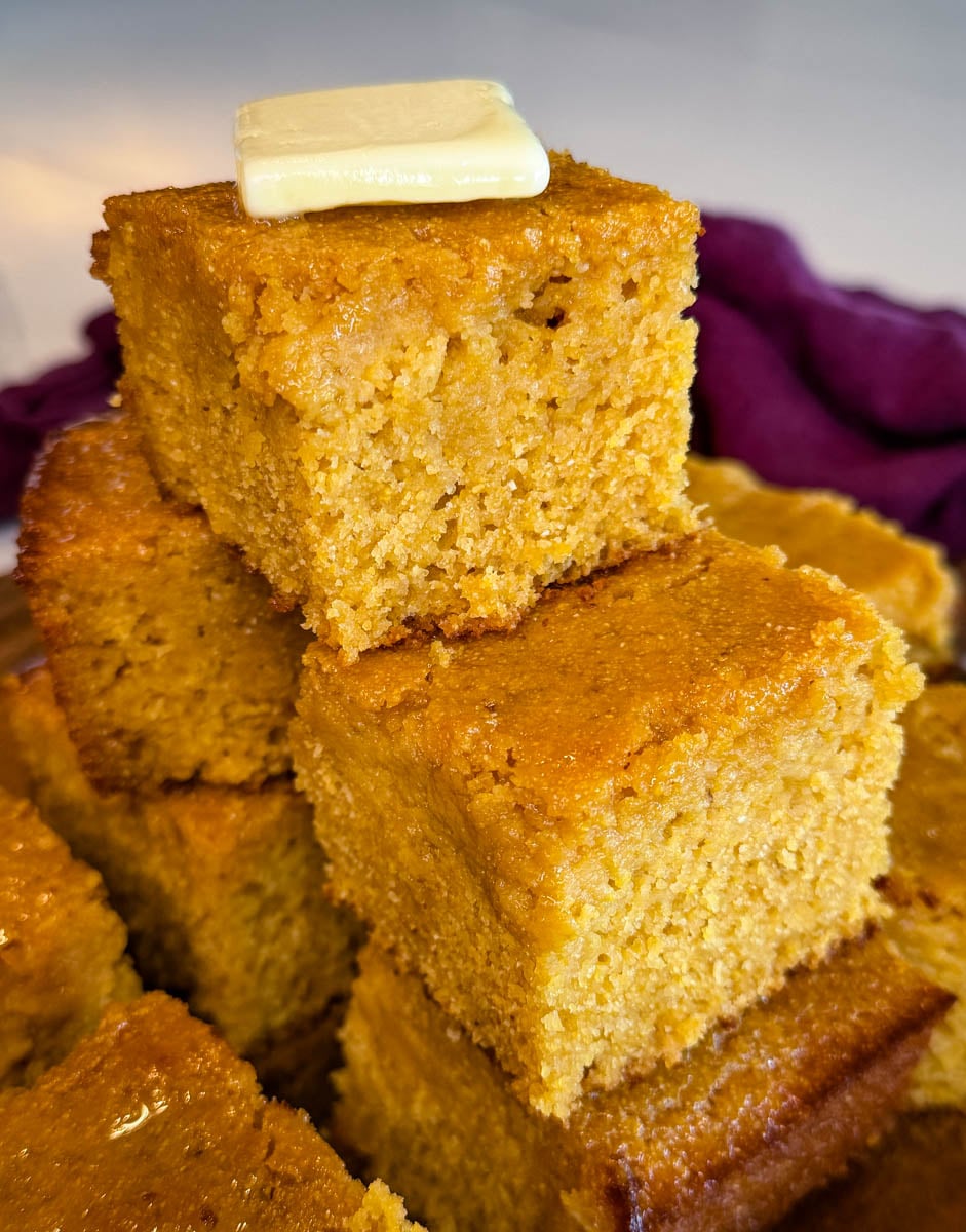 Thick slice of honey butter cornbread topped with butter, showcasing the soft, moist interior and golden edges.