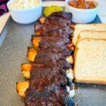 BBQ beef ribs served with coleslaw, pickles, and white bread on a plate.