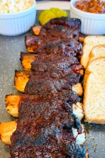 BBQ beef ribs served with coleslaw, pickles, and white bread on a plate.