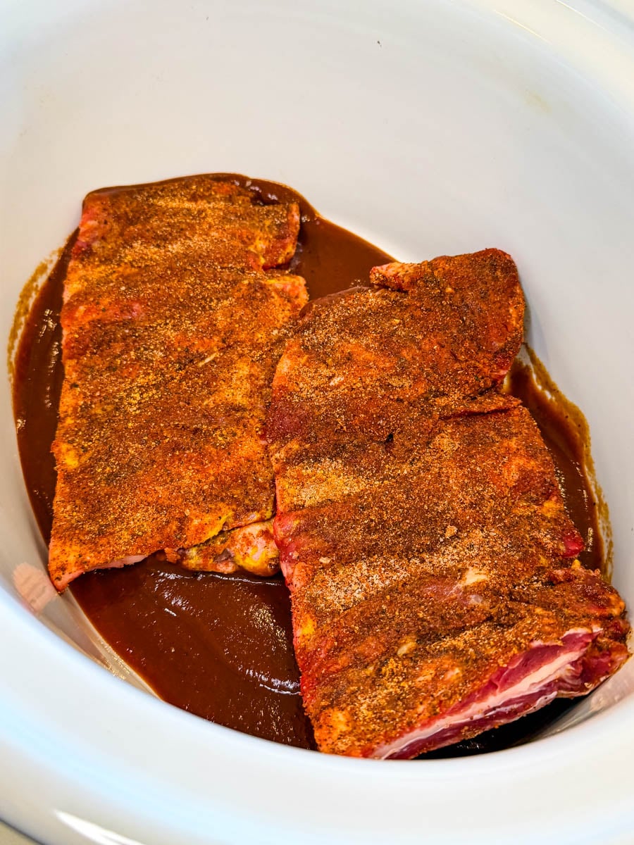 Seasoned beef ribs placed in a slow cooker with BBQ sauce before cooking.