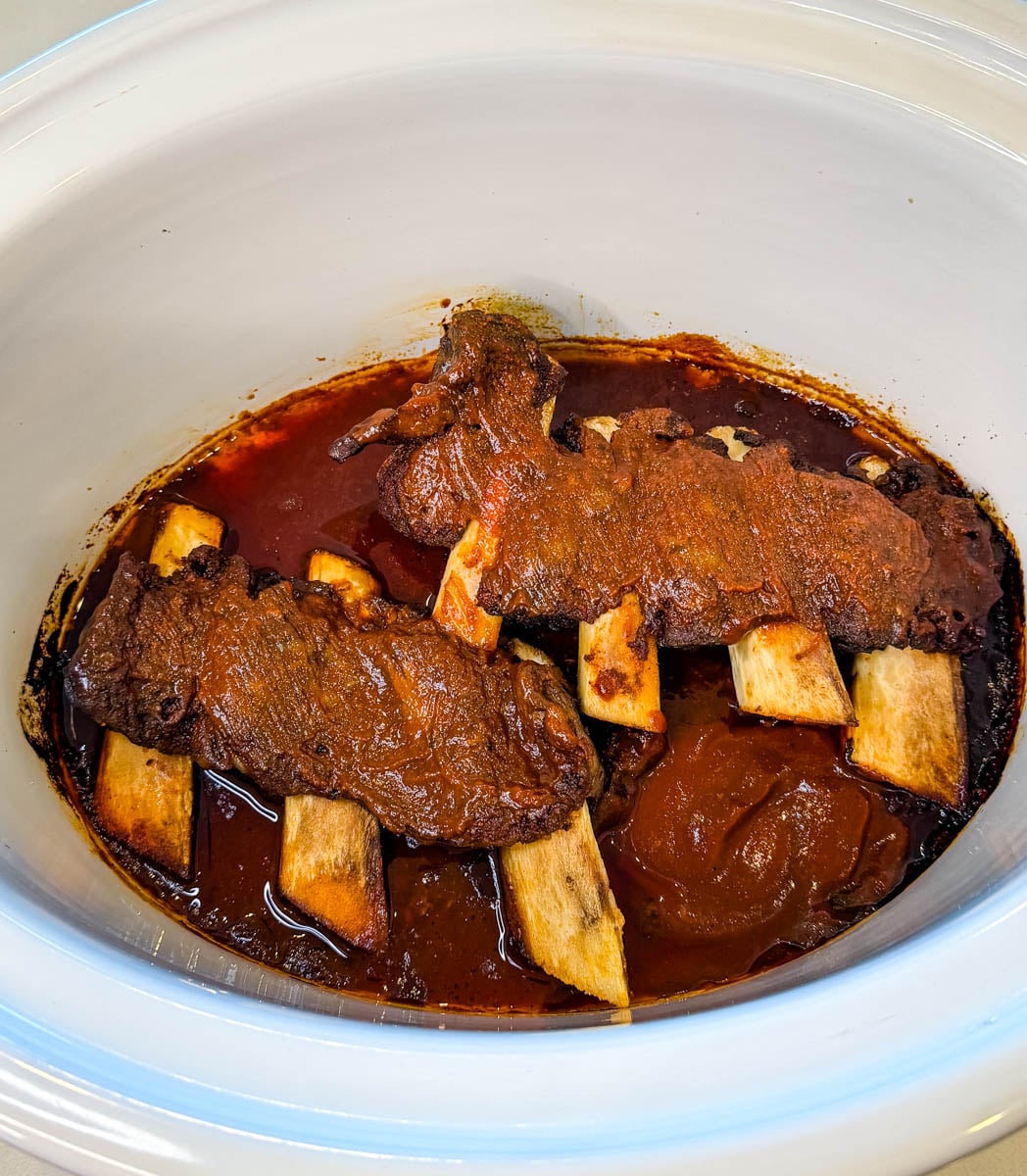 Slow cooker beef ribs cooked in BBQ sauce inside a white Crockpot.