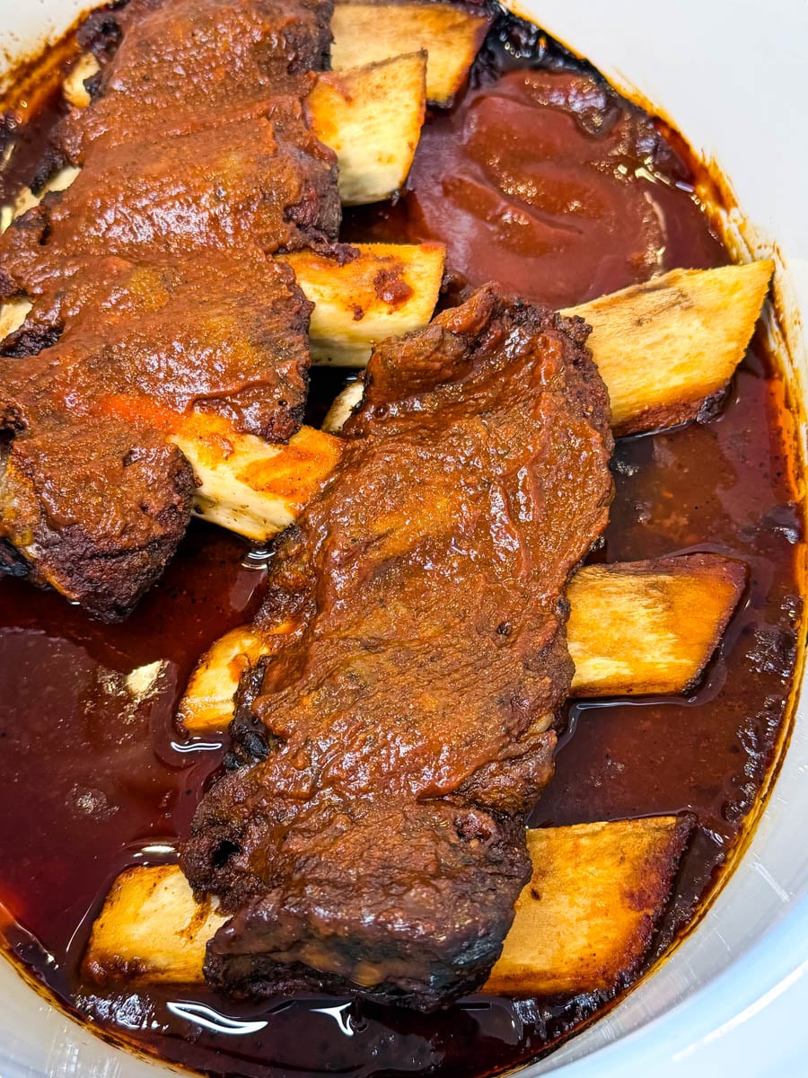 Close-up of tender beef ribs in the slow cooker covered in BBQ sauce.