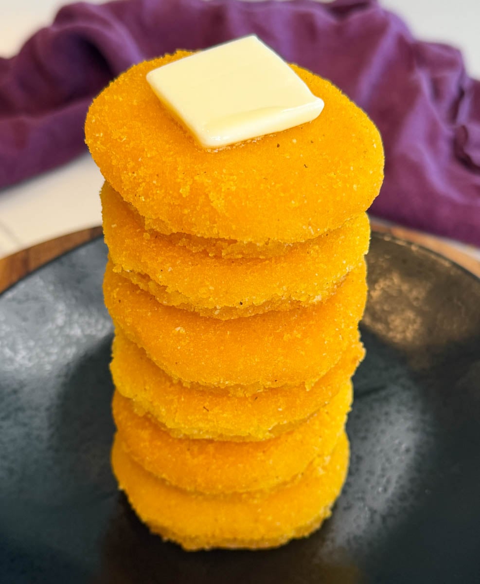 Close-up of stacked hot water cornbread with crisp golden edges and butter melting on top.