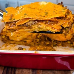 Close-up of a cheesy beef enchilada casserole showing layers of corn tortillas, seasoned ground beef, melted cheese, enchilada sauce, and corn.