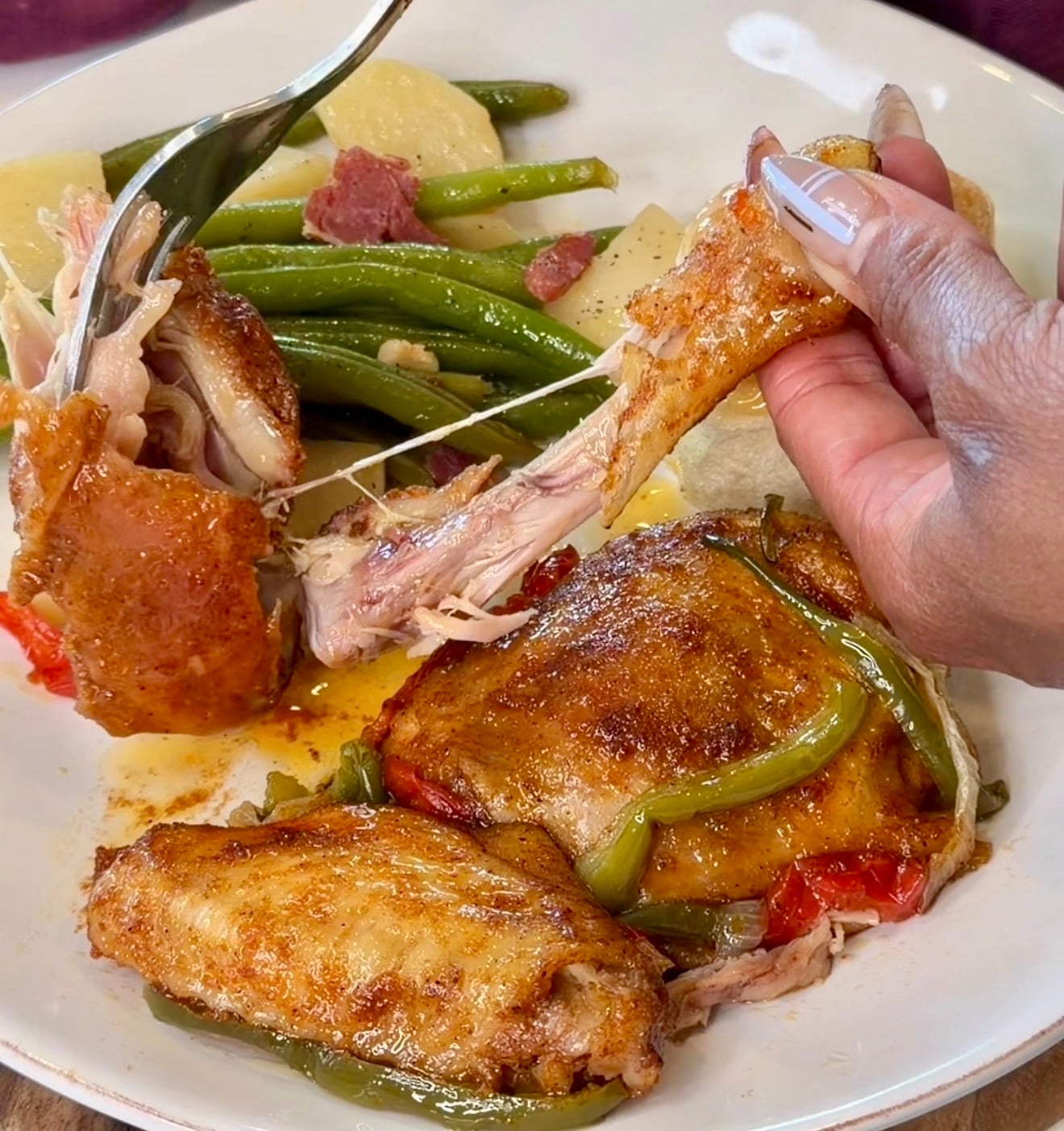 person holding baked chicken drumstick with meat falling off the bone using a fork.