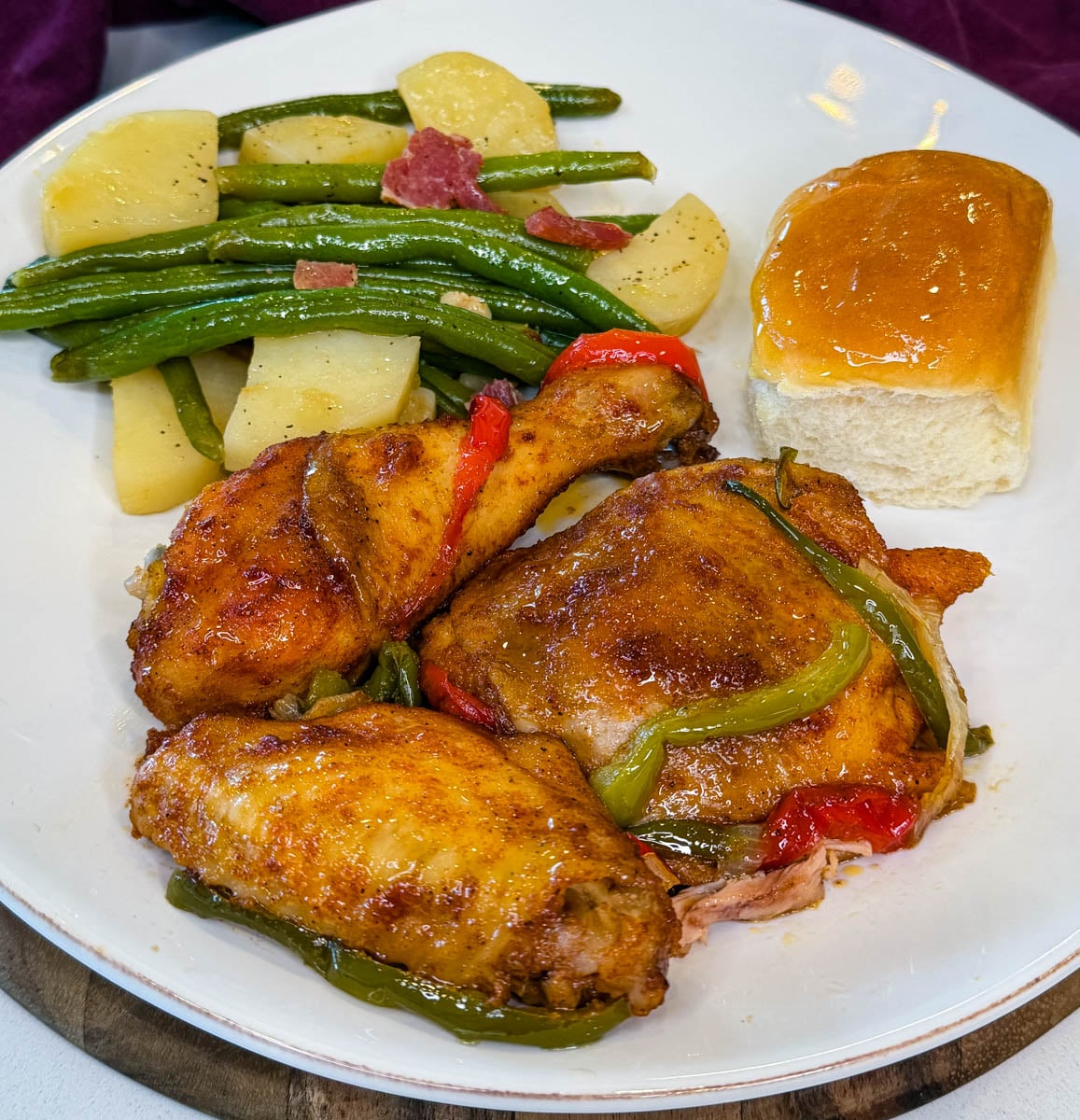 Southern baked chicken served with green beans, potatoes, and a dinner roll, topped with tender bell peppers and onions.