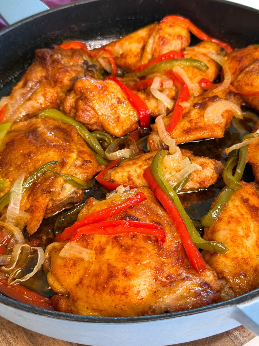 Baked chicken thighs, wings, and drumsticks baked with sliced red and green bell peppers and onions in a cast iron skillet.