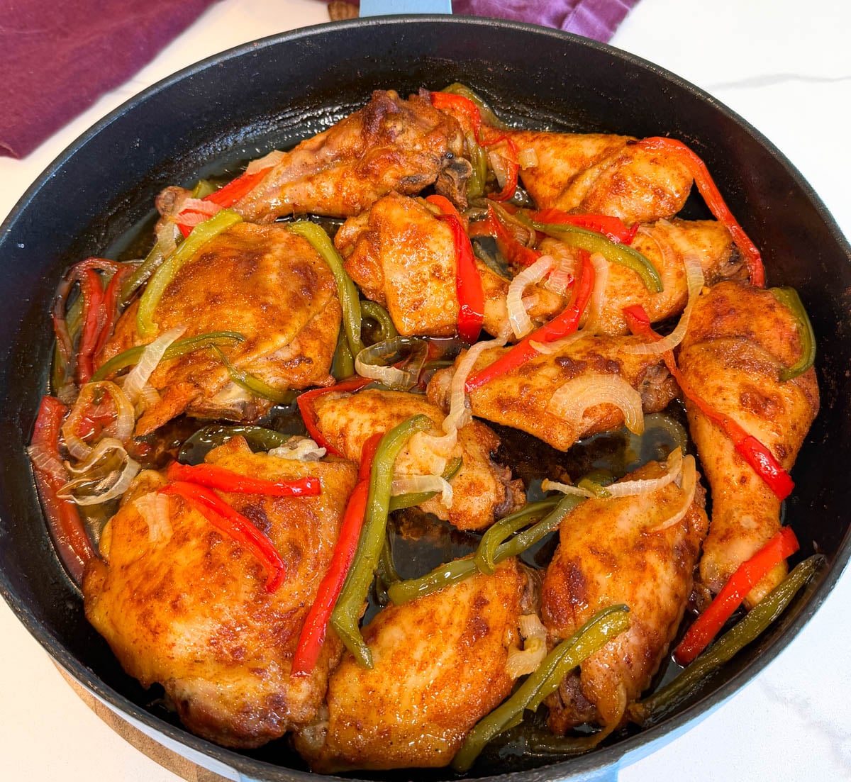 Cast iron skillet filled with golden brown baked chicken, bell peppers, and onions in a savory pan sauce.