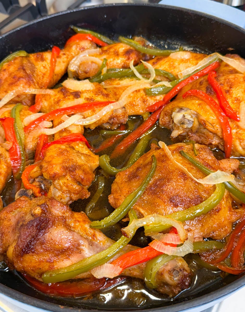 Close-up of juicy baked chicken pieces topped with tender onions and red and green bell peppers in a rich pan gravy.