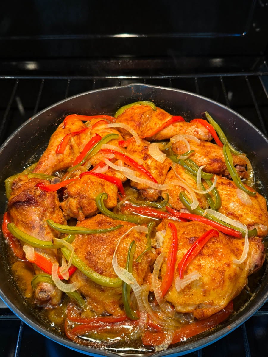 Baked chicken roasting in the oven with bell peppers and onions, surrounded by flavorful cooking juices.