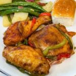 Southern baked chicken served with green beans, potatoes, and a dinner roll, topped with tender bell peppers and onions.