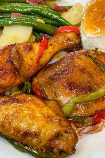 Southern baked chicken served with green beans, potatoes, and a dinner roll, topped with tender bell peppers and onions.