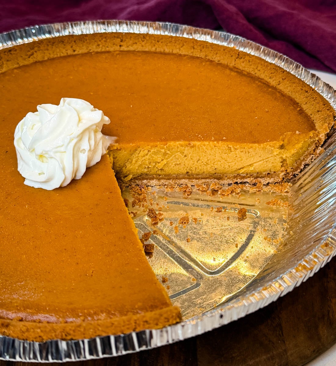 Close-up of a baked sweet potato pie with a graham cracker crust showing a creamy filling and a slice removed, topped with whipped cream.