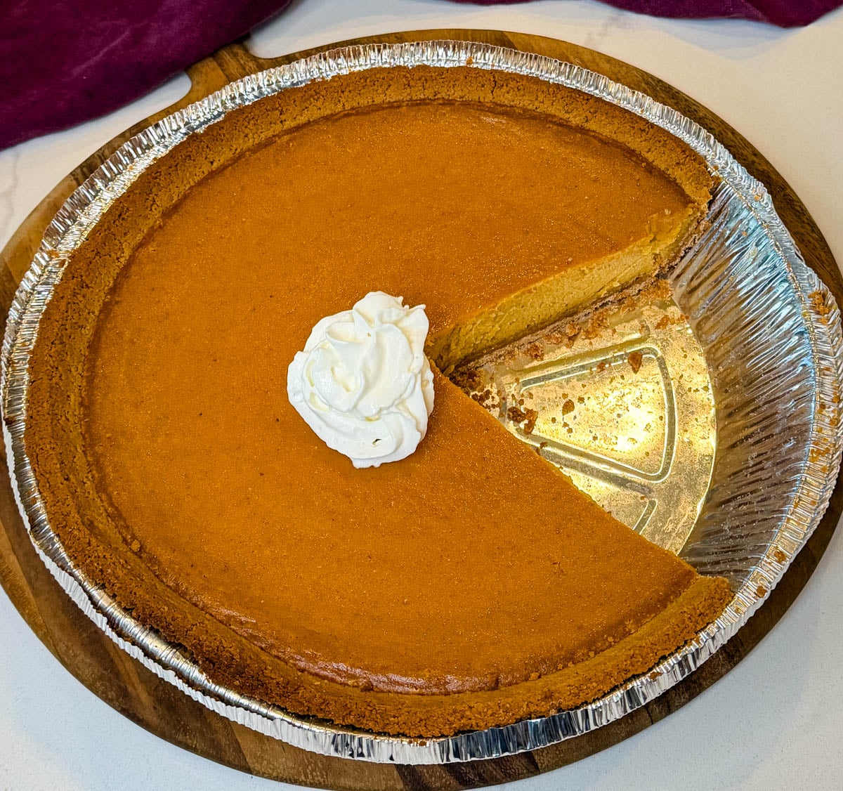 Close-up of a baked sweet potato pie with a graham cracker crust showing a creamy filling and a slice removed, topped with whipped cream.