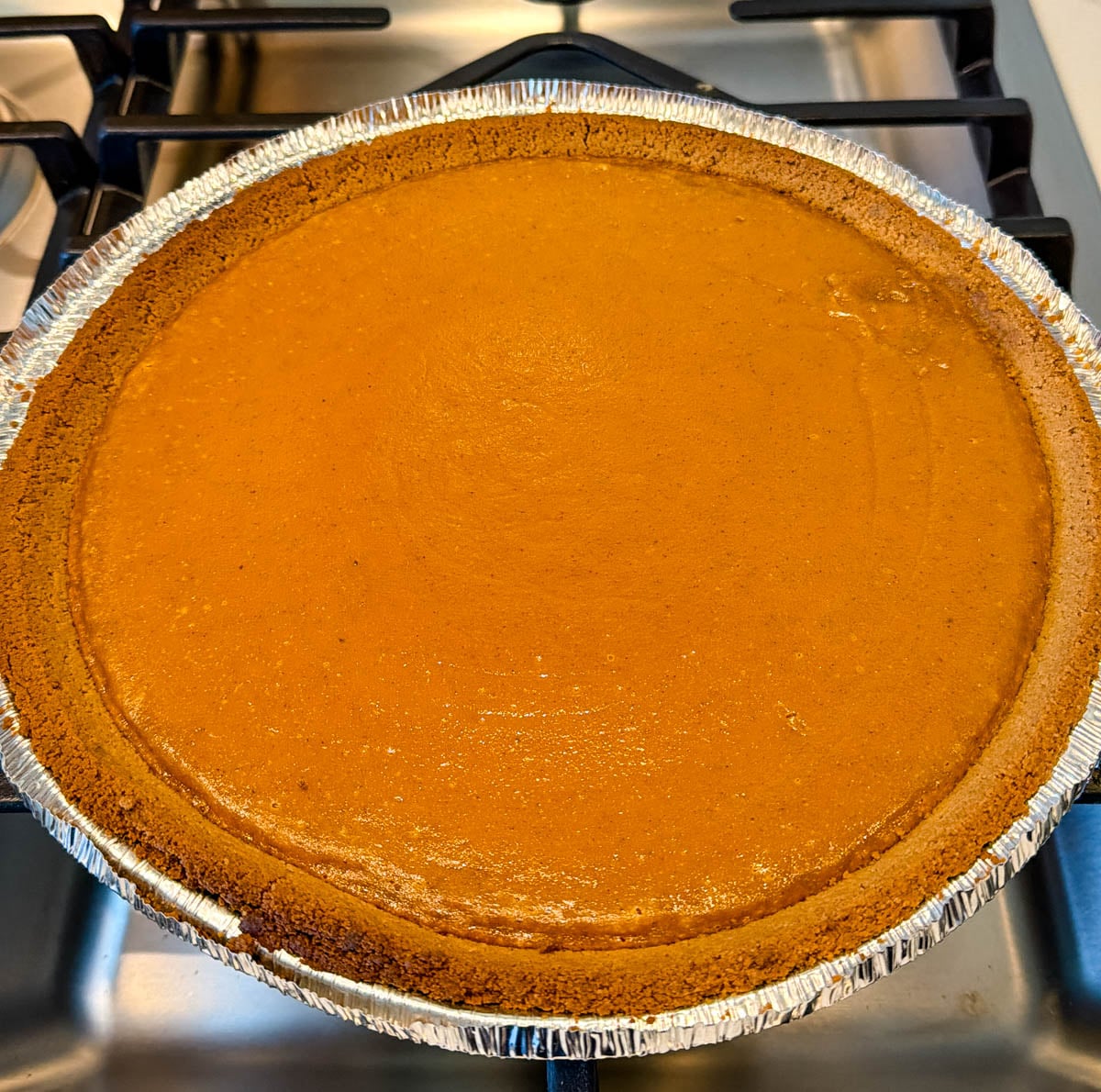 Freshly baked sweet potato pie with a graham cracker crust cooling in a disposable pie pan on a stovetop.