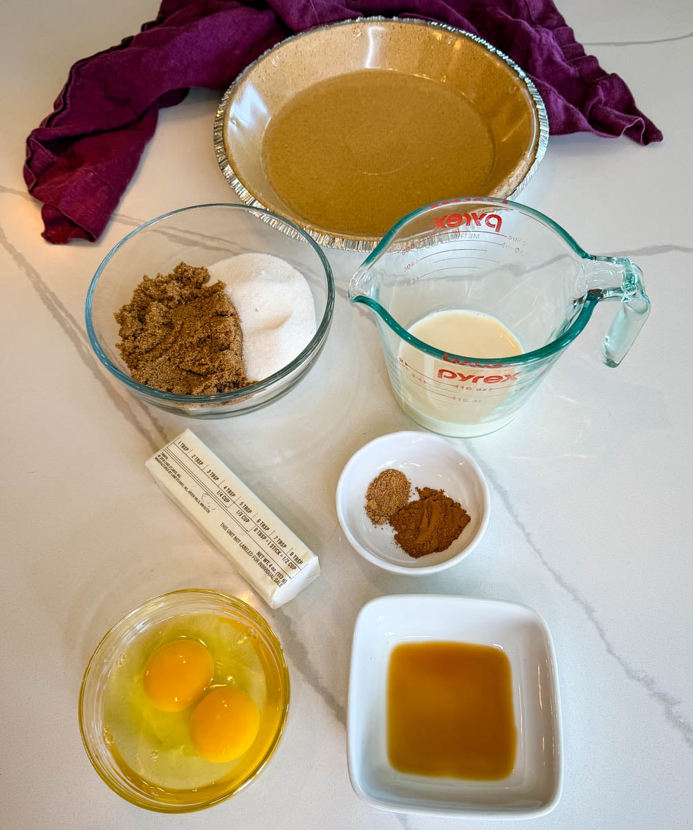 Ingredients for sweet potato pie with a graham cracker crust including eggs, evaporated milk, butter, brown sugar, granulated sugar, vanilla, cinnamon, nutmeg, and a prepared graham cracker crust.