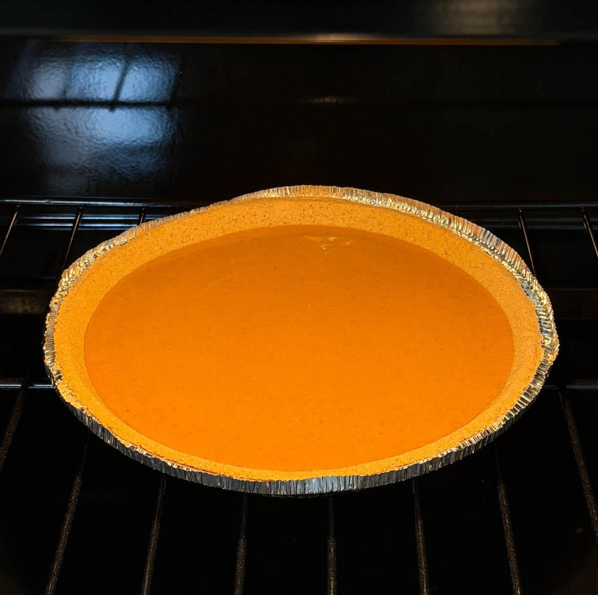 Sweet potato pie baking in the oven in a prepared graham cracker crust until the filling is set.