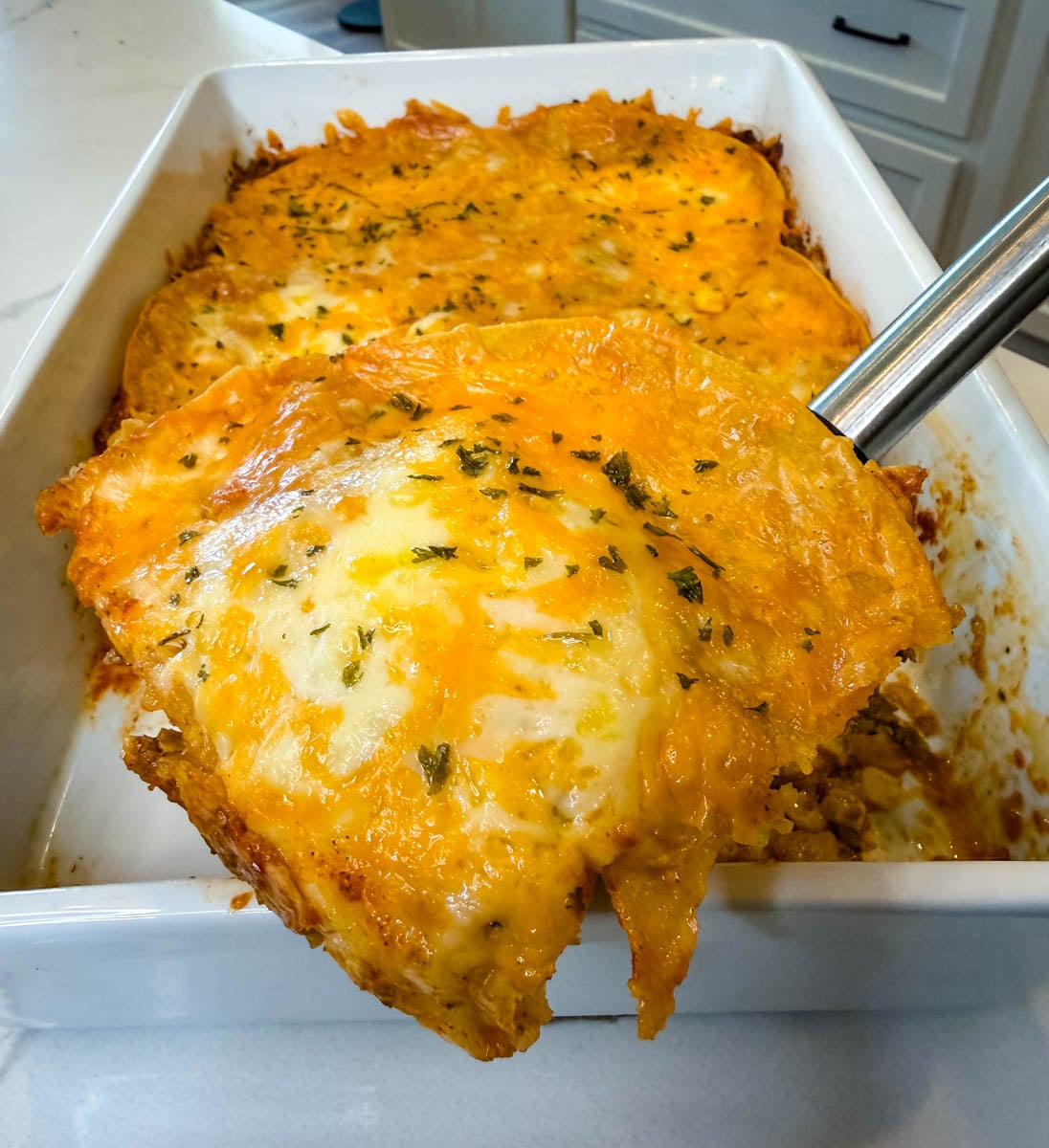 Close-up of a cheesy beef enchilada casserole showing layers of corn tortillas, seasoned ground beef, melted cheese, enchilada sauce, and corn.