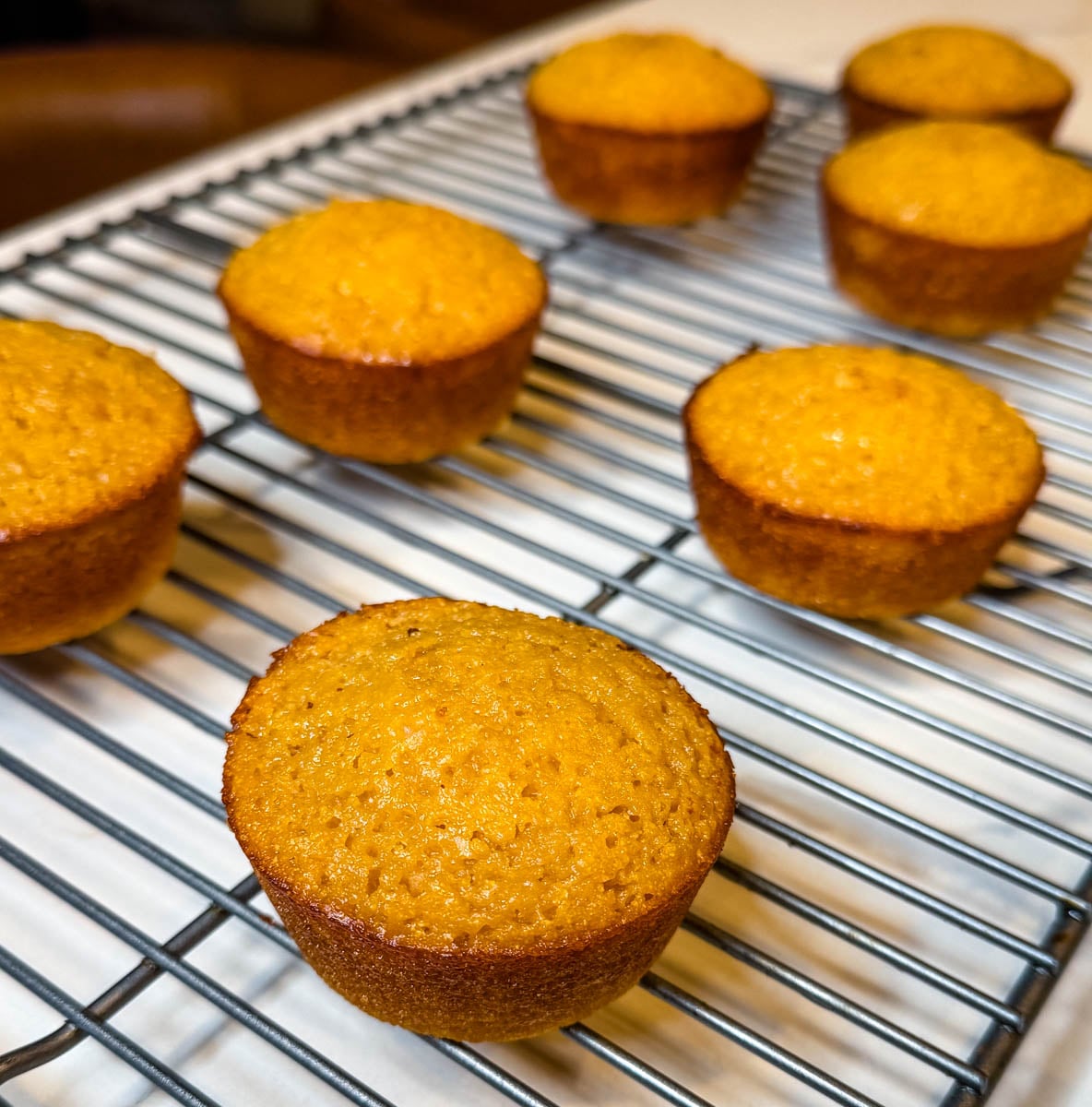 Freshly baked honey butter cornbread muffins cooling on a wire rack, with golden tops and crisp browned edges.