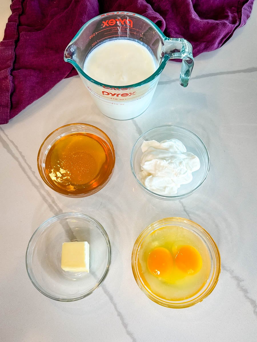 Ingredients for honey butter cornbread muffins including buttermilk, honey, sour cream, butter, and eggs arranged on a countertop.