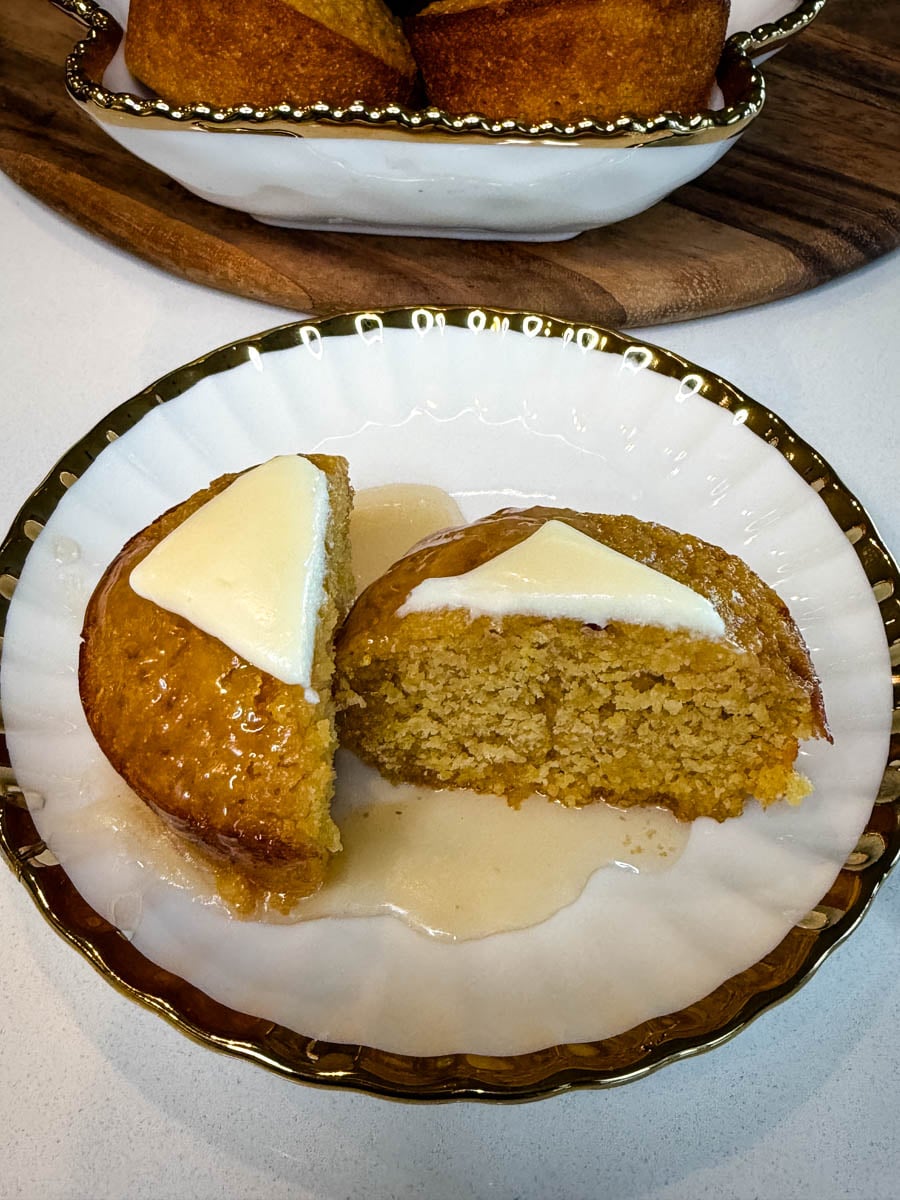 Honey butter cornbread muffin sliced in half and topped with butter, served on a white plate with honey drizzled around the muffin.