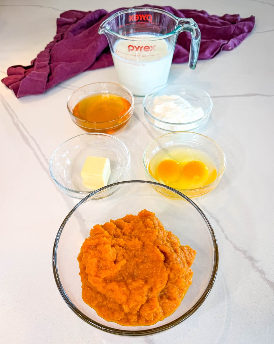 Ingredients for sweet potato honey cornbread muffins including sweet potato puree, milk, honey, sour cream, butter, and eggs arranged on a countertop.