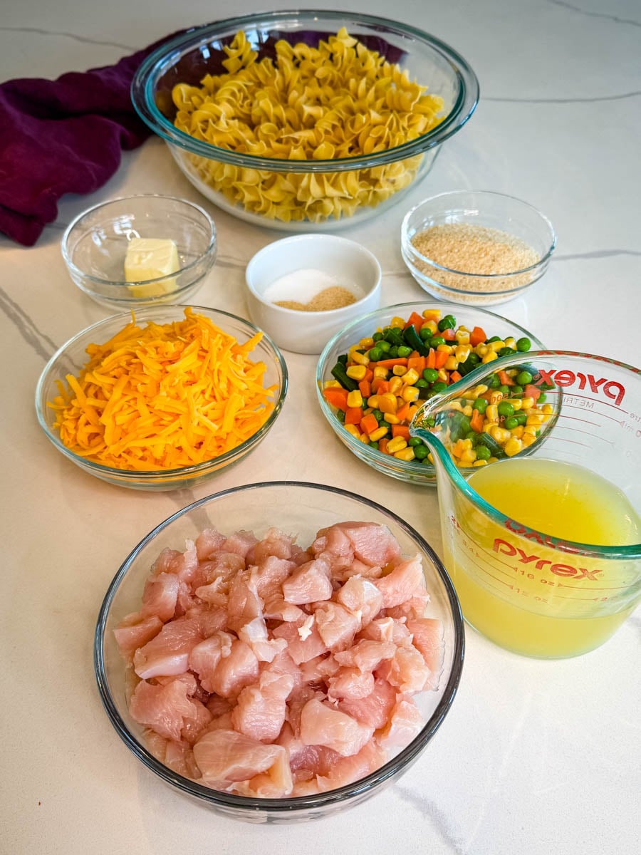 Chicken noodle casserole ingredients including diced chicken breast, egg noodles, mixed vegetables, shredded cheddar cheese, chicken broth, breadcrumbs, butter, and seasonings.