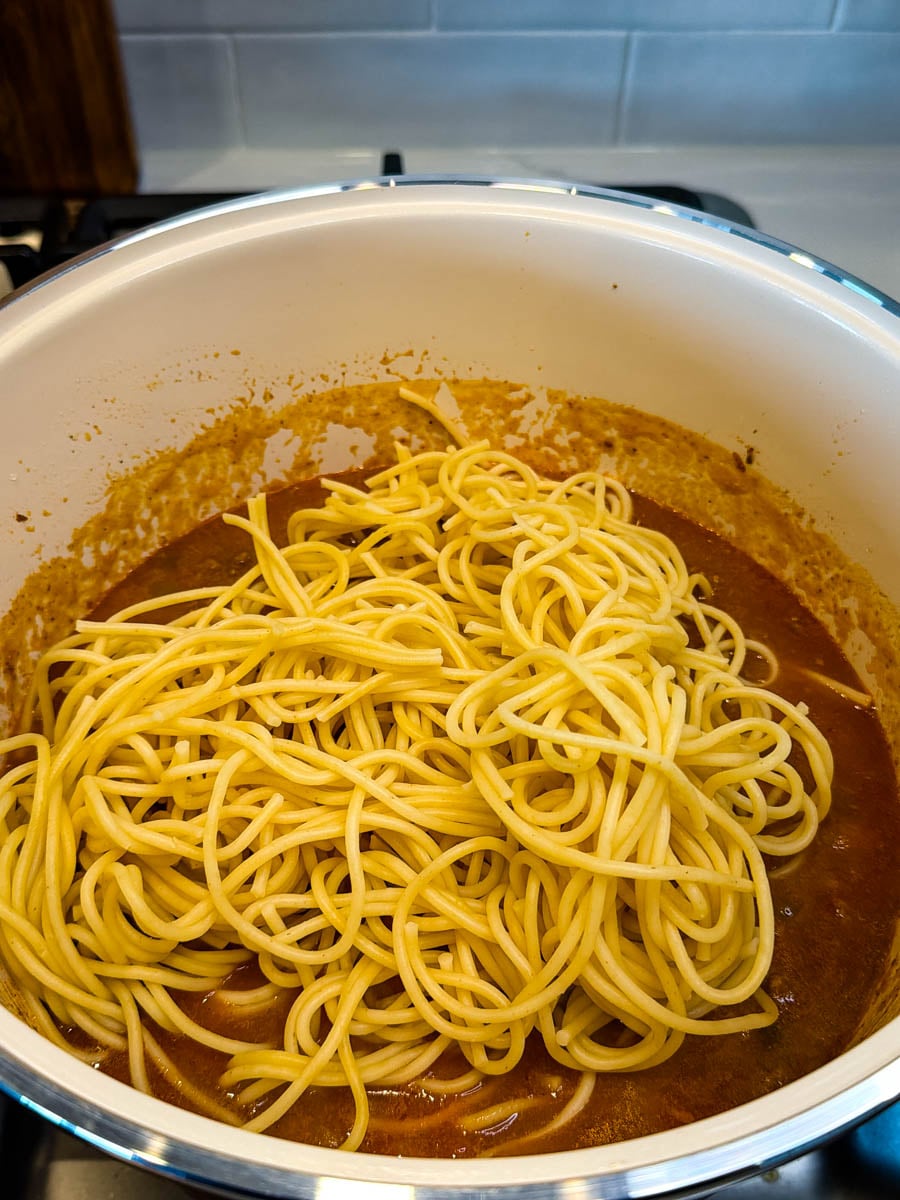 Cooked spaghetti noodles added to a pot of seasoned tomato sauce before being tossed with the meat mixture.