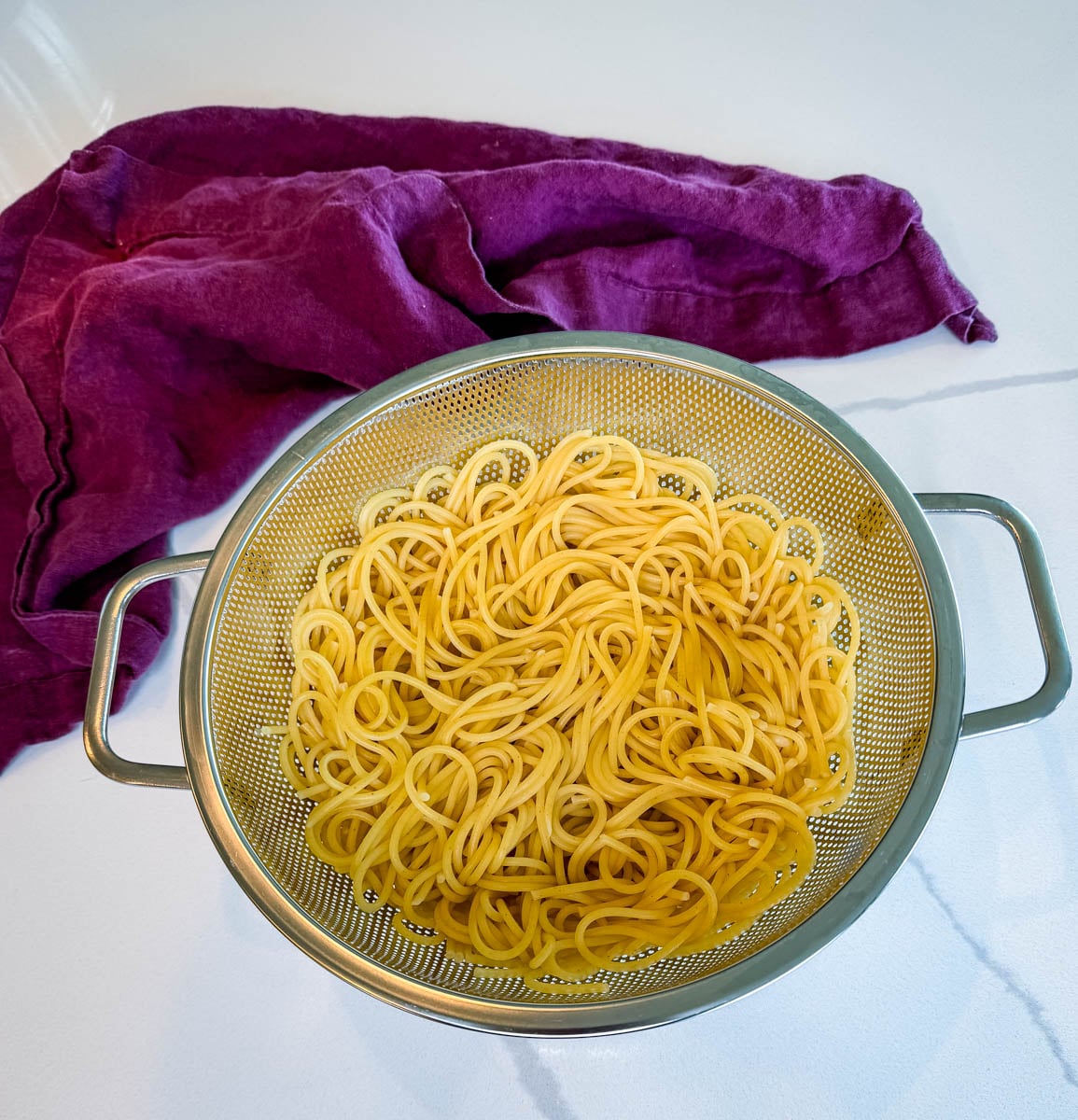 Cooked spaghetti noodles draining in a metal colander after boiling.
