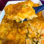 Close-up of creamy chicken noodle casserole with tender noodles, chicken, mixed vegetables, melted cheddar cheese, and a golden breadcrumb topping served on a spoon.