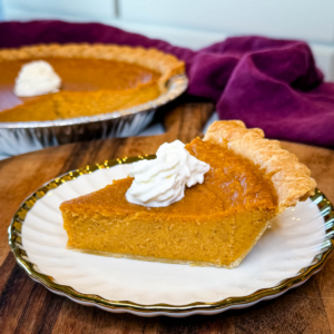 Slice of Southern sweet potato pie in a flaky store-bought crust topped with whipped cream, with the remaining pie in the background.