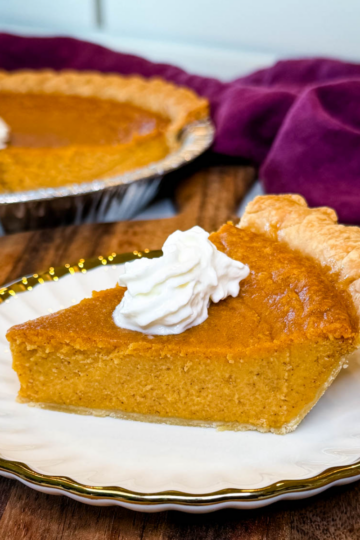 Slice of Southern sweet potato pie in a flaky store-bought crust topped with whipped cream, with the remaining pie in the background.