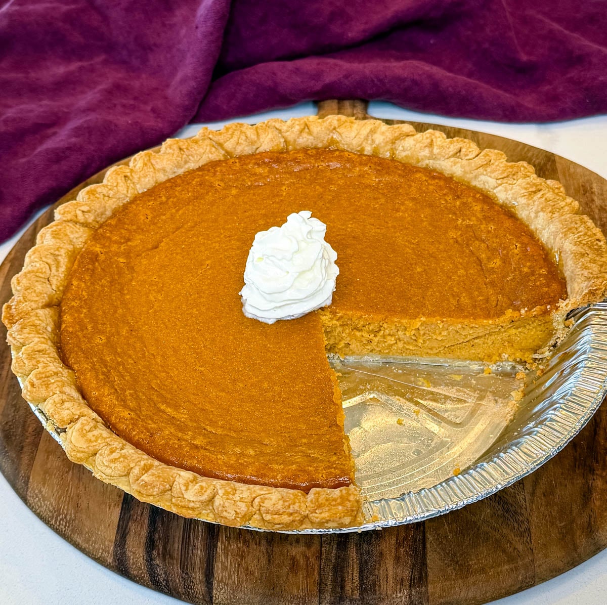 Whole Southern sweet potato pie baked in a store-bought crust with one slice removed and whipped cream in the center.