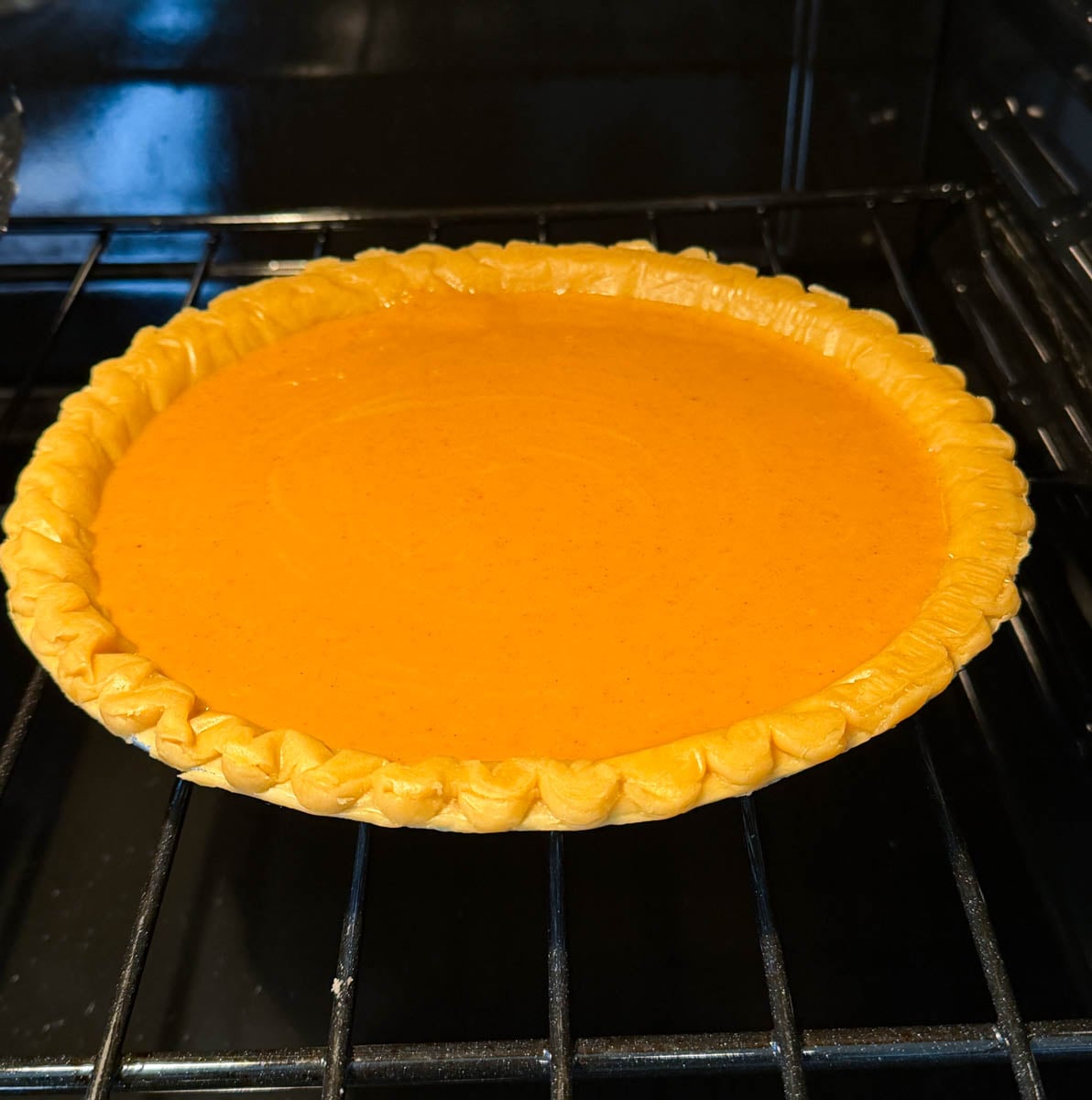 Unbaked sweet potato pie with smooth orange filling in a store-bought crust sitting on an oven rack.