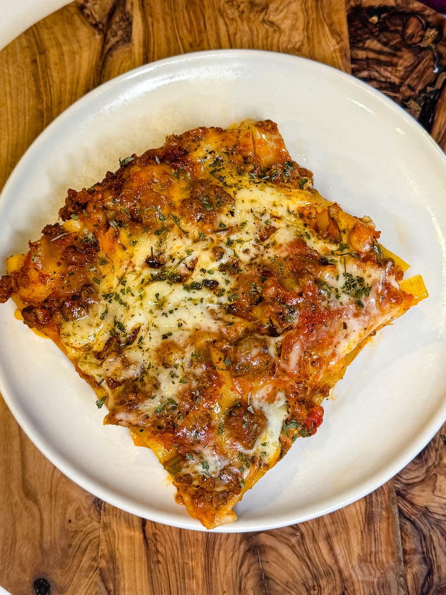 Slice of homemade slow cooker lasagna with layers of pasta, seasoned meat sauce, melted cheese, and herbs served on a white plate.