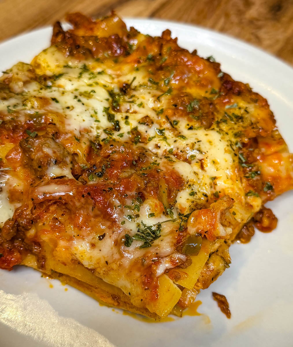 Close-up of Crockpot lasagna with tender noodles, rich meat sauce, gooey melted cheese, and Italian herbs on a white plate.