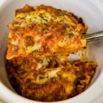 Close-up of a thick slice of slow cooker lasagna with layers of pasta, meat sauce, and melted cheese being lifted from the Crockpot.