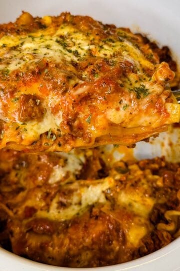 Close-up of a thick slice of slow cooker lasagna with layers of pasta, meat sauce, and melted cheese being lifted from the Crockpot.