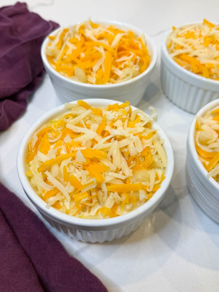 Individual ramekins filled with creamy macaroni and cheese and topped with freshly shredded cheddar cheese before air frying.