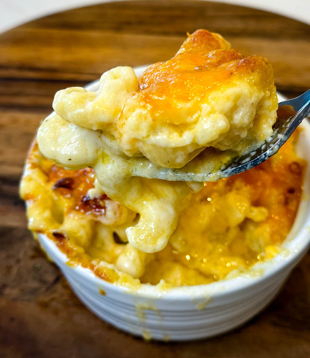 Spoonful of creamy air fryer macaroni and cheese lifted from a ramekin, showing tender pasta and gooey melted cheese.