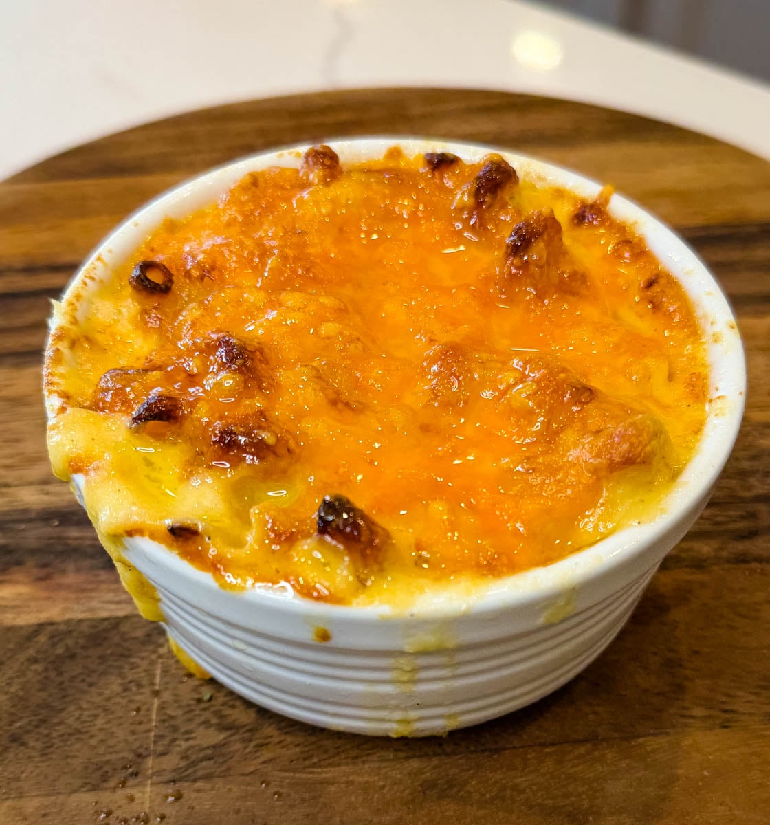 Individual serving of air fryer mac and cheese with a golden, bubbly cheese crust in a white ramekin.