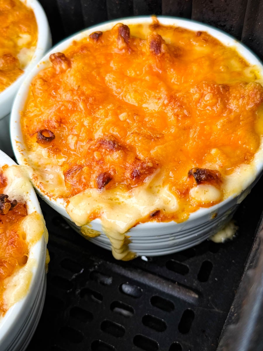 Close-up of baked macaroni and cheese in the air fryer with melted cheddar cheese bubbling over the edge of the ramekin.