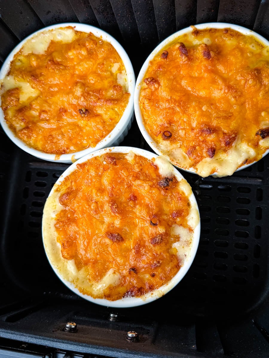 Freshly cooked air fryer macaroni and cheese in three ramekins with bubbling golden cheese on top.
