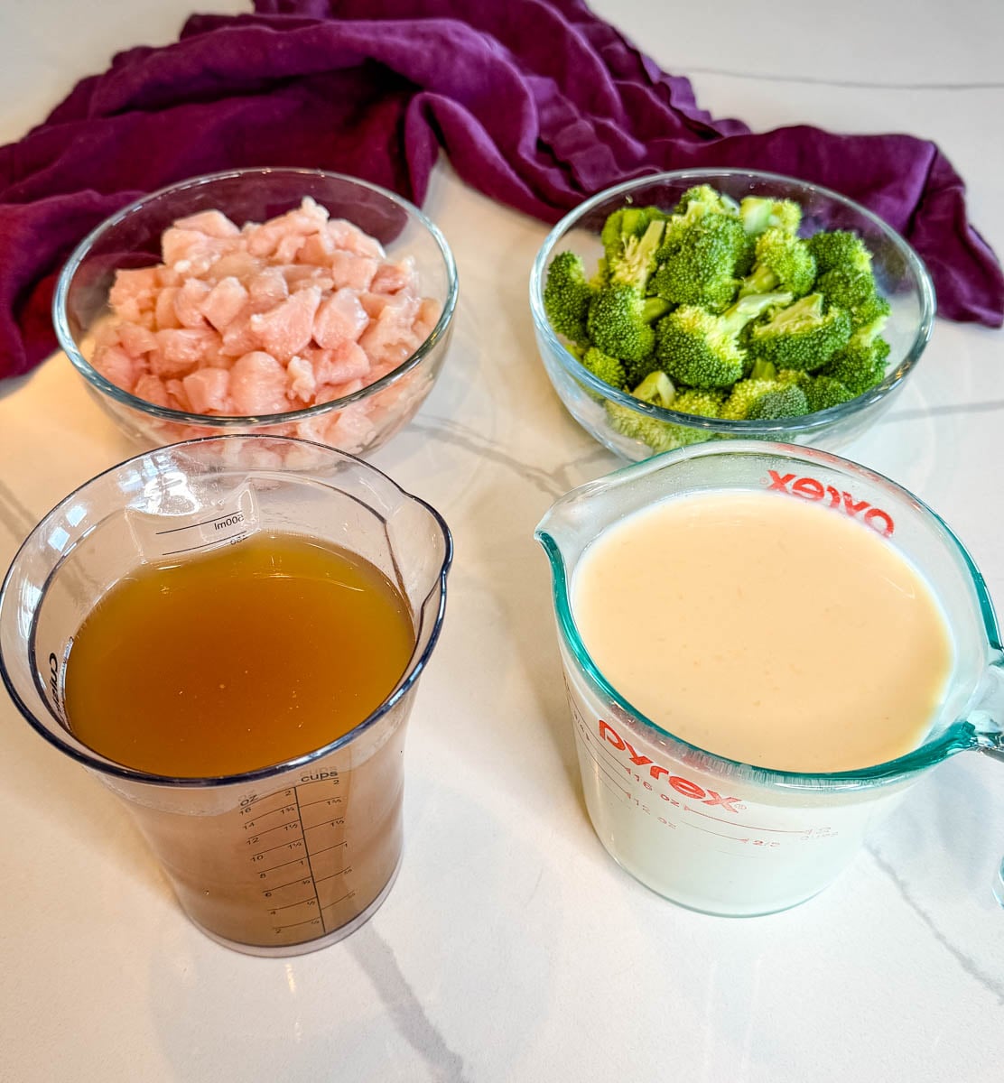Chicken broccoli rice casserole ingredients with diced raw chicken, fresh broccoli florets, chicken broth, and creamy soup mixture.