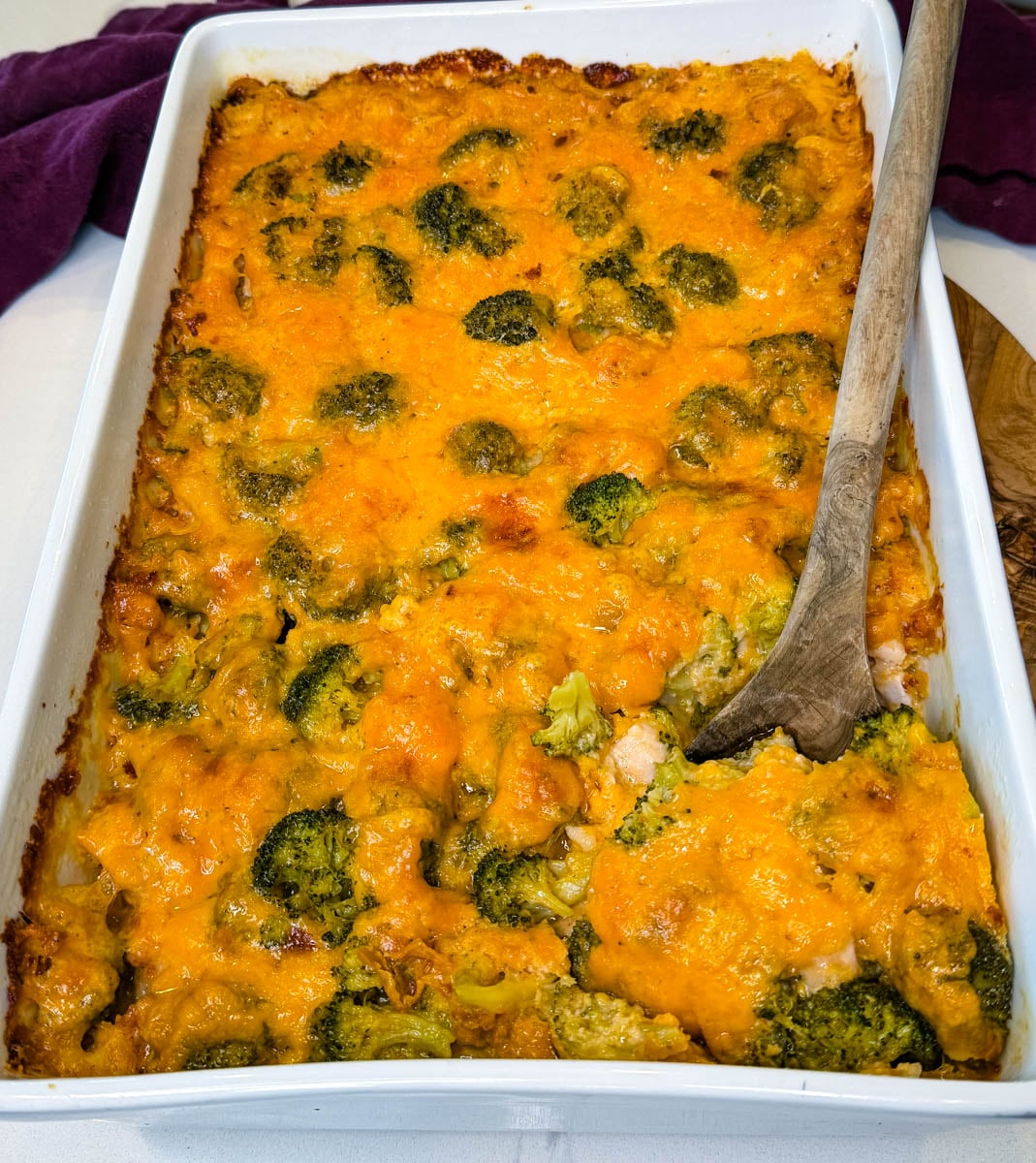 Finished chicken broccoli rice casserole in a white baking dish topped with golden melted cheddar cheese and broccoli florets.