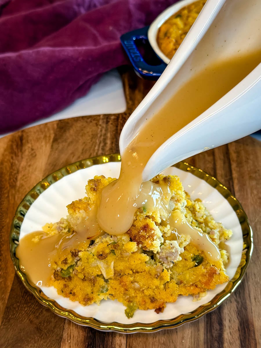 Southern cornbread dressing with sausage served on a plate while savory gravy is poured over the top.