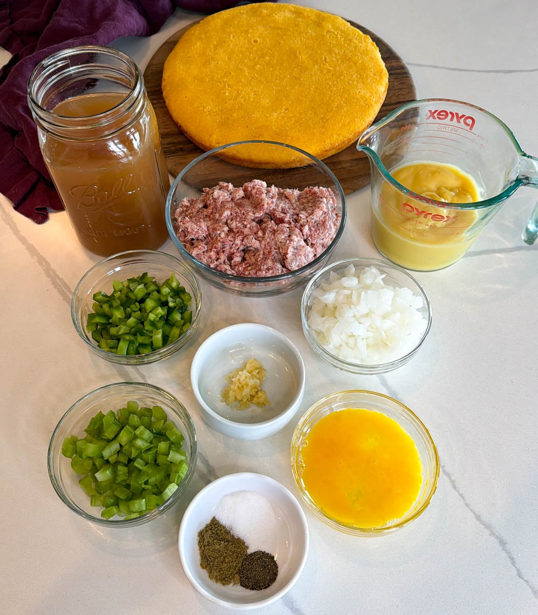 Ingredients for homemade cornbread dressing with sausage, including cornbread, sausage, broth, cream soup, onions, green peppers, celery, garlic, eggs, and seasonings.