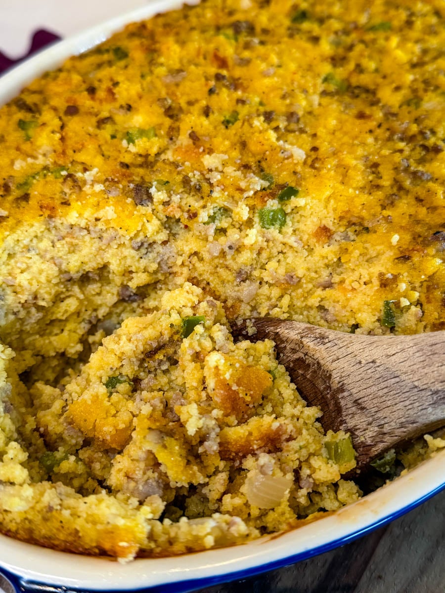 Close-up of homemade cornbread dressing with sausage, onions, and green peppers being scooped from a baking dish.