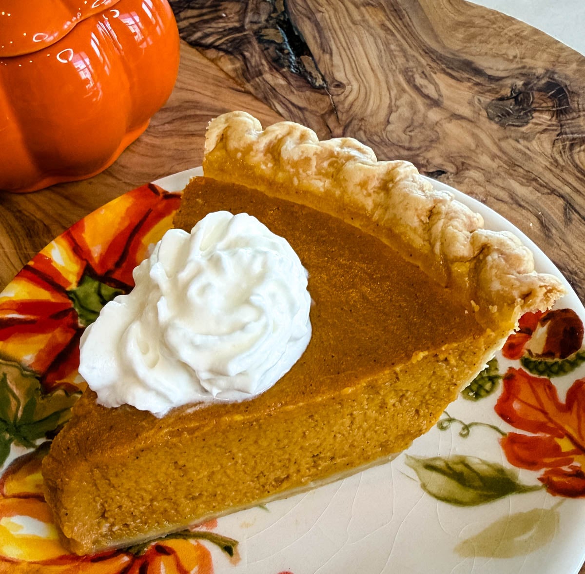 Close-up of a slice of creamy pumpkin pie made with a frozen crust and topped with a generous swirl of whipped cream.